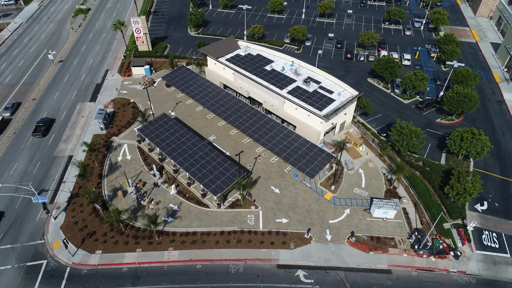 Aerial of the wash: two long solar canopies over the vacuum bays, panels on the white building roof, Balboa Avenue alongside
